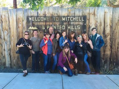 A group of people under the town sign leaning against a fence